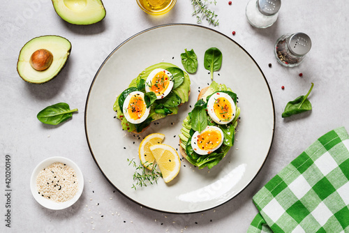 Healthy toast with sliced avocado, boiled eggs, spices and fresh spinach. Delicious breakfast or snack on gray stone background. top view