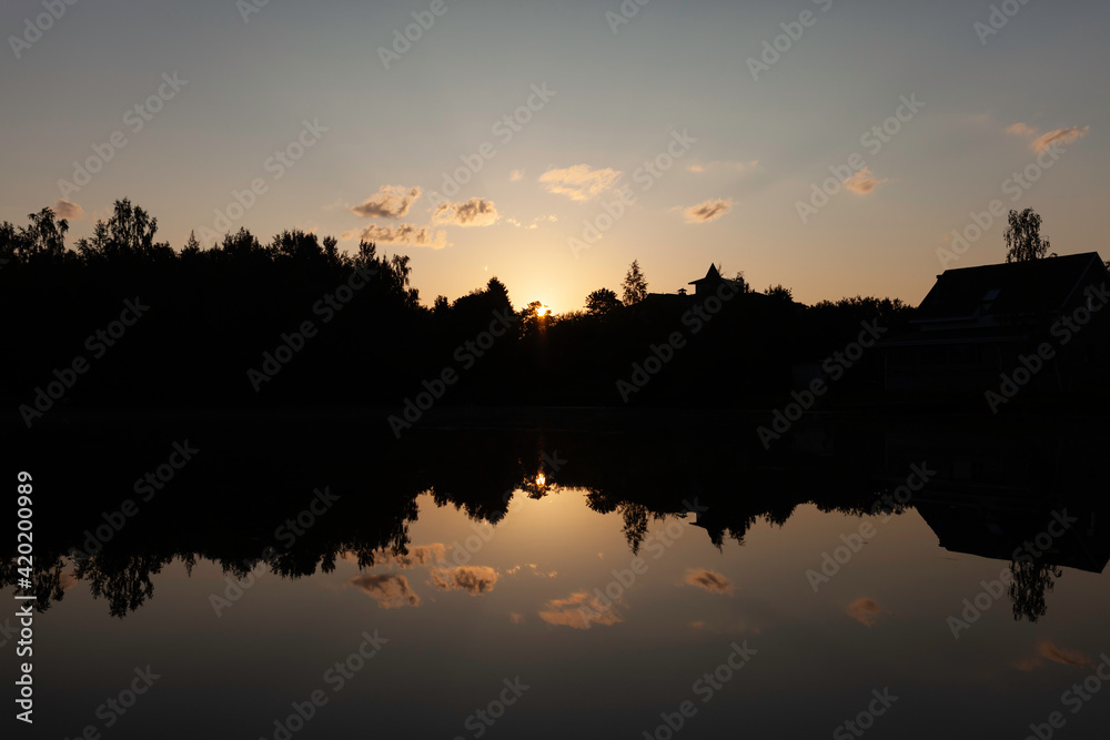 sunrise over the lake with the reflection of trees, houses and pink clouds in the smooth surface of the water. peace and quiet, tranquility, the birth of the day