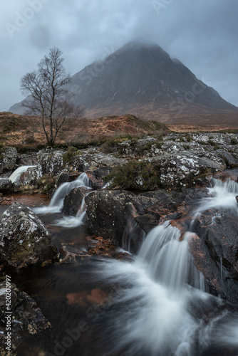 Epic landscape image of Buachaille Etive Mor waterfall in Scottish highlands on a Winter morning with long exposure for smooth flowing water