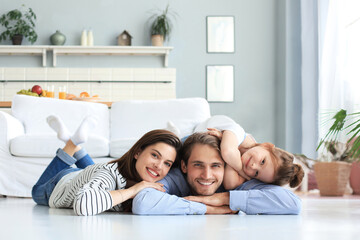 Young Caucasian family with small daughter pose relax on floor in living room, smiling little girl kid hug embrace parents, show love and gratitude, rest at home together.