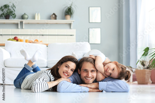 Young Caucasian family with small daughter pose relax on floor in living room, smiling little girl kid hug embrace parents, show love and gratitude, rest at home together.