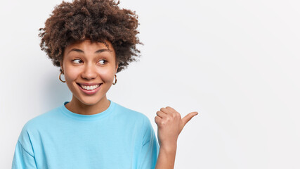 Horizontal shot of cute pleased Afican American woman shows store promo deal smiles positively points at right copy space isolated over white background shares good news with you. Check this out