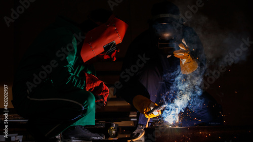 mechanics workers work overtime hardly at night in a factory. Engineers wearing safety outfits with mechanic jumpsuits, gloves, boots, and welding helmets working on metal welding