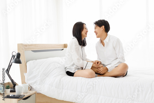 LGBTQ couple lovers, a handsome girl as man or butch and femme, spending and sharing loving time in white bedroom with fun, warmth, and happiness