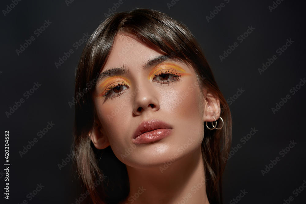 Beautiful face of young brunette woman with colorful bright makeup looking at camera isolated over black background Beautiful face of young brunette woman with colorful bright makeup looking at camera isolated over black background