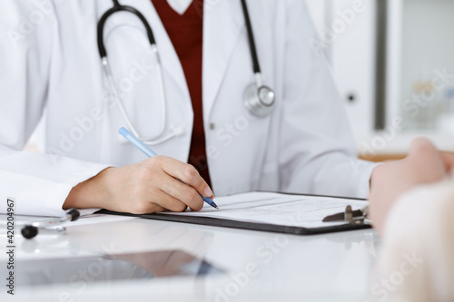 Unknown woman-doctor filling up an application form while consulting patient. Medicine concept