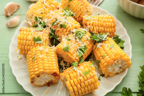 Plate with tasty baked corn cobs on color wooden background