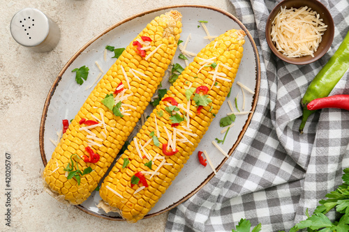 Plate with tasty baked corn cobs on light background