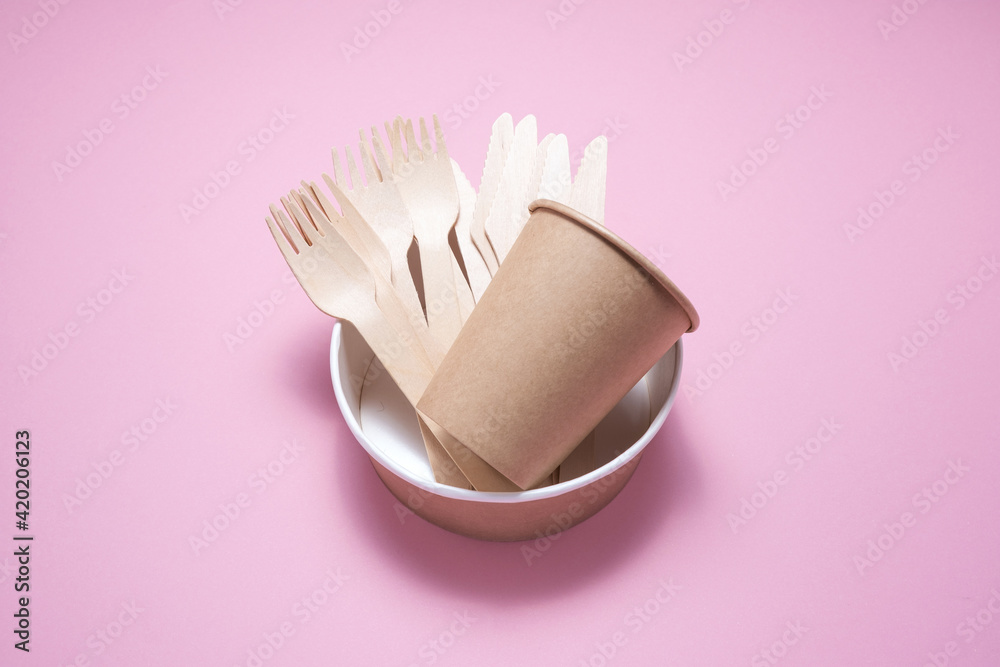 Wooden and cardboard disposable tableware on a pink background. Environmentally friendly products.