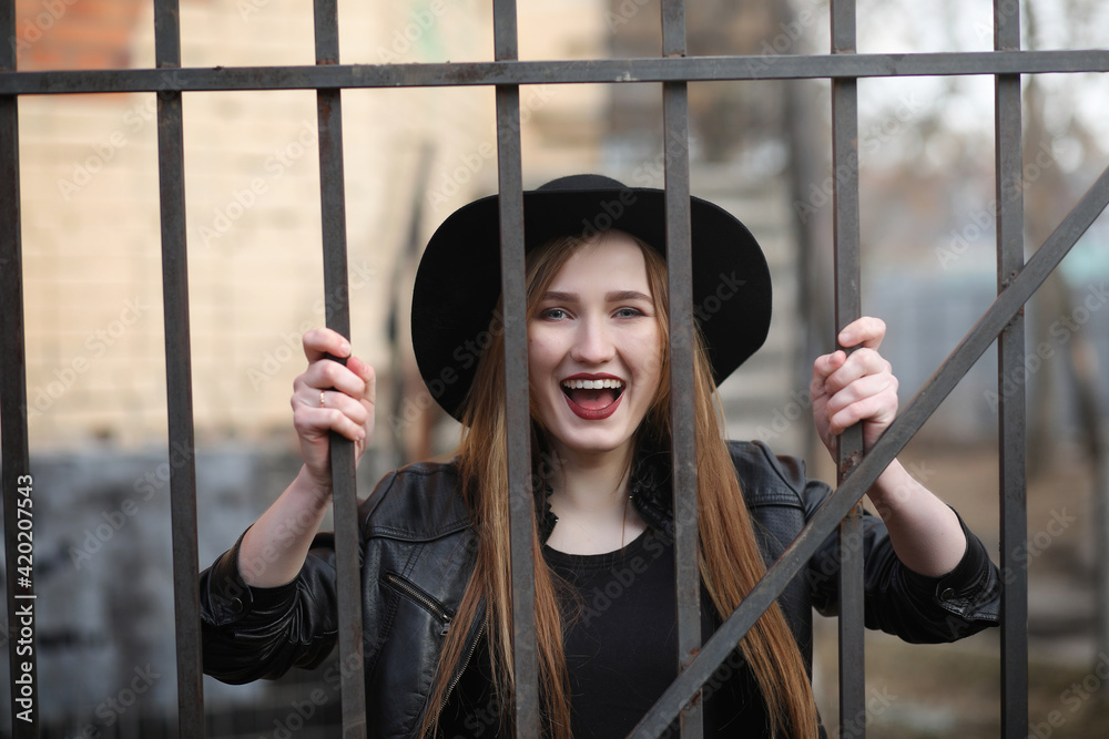 Obraz premium A girl walks down the city street in a leather waistcoat with a phone. Young beautiful girl in a hat and with a dark make-up outside. Girl in the Gothic style on street.