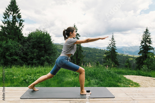 Young fit woman stretching or doing squats on yoga mat at sunny mountains. Outdoor healthy workout