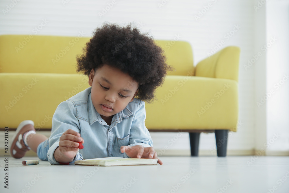 Little African boy holding red crayon in hand drawing coloring on book and lying on the floor at home Little African boy holding red crayon in hand drawing coloring on book and lying on the floor at home