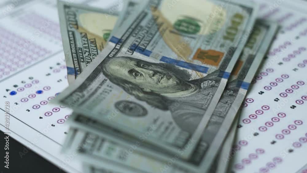 Corruption in exams. Corruption in education. Education and exam concept. US dollars on the exam test paper. A student putting on money on the test sheet Corruption in exams. Corruption in education. Education and exam concept. US dollars on the exam test paper. A student putting on money on the test sheet