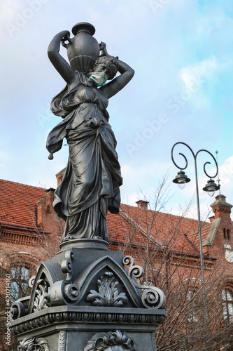 MYSLENICE, POLAND - MARCH 06, 2021: The girl statue in the fountain with the coronavirus mask on her face, at the main market square