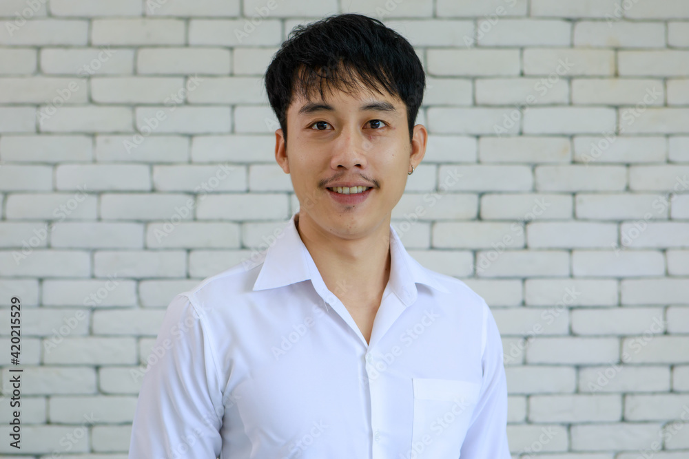 Portrait of young and handsome Asian man with beard pose smile and happy friendly face on white brick wall background Portrait of young and handsome Asian man with beard pose smile and happy friendly face on white brick wall background