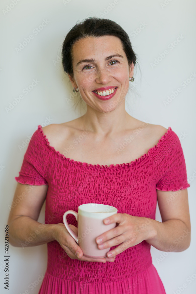 Beautiful smiling woman in pink dress holds cup in her hands Beautiful smiling woman in pink dress holds cup in her hands
