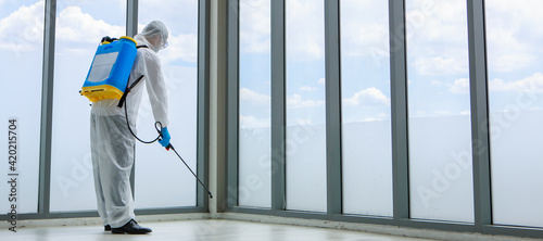 Officer wearing sterilize protective suit with chemical tank on back spraying Disinfectant solution in office place to reduce and protect coronavirus