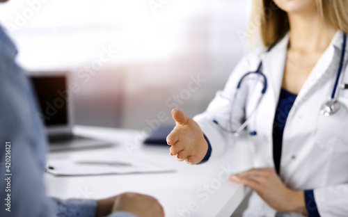 Unknown woman-doctor is talking to her patient  while they are sitting together in the sunny cabinet in a clinic. Female physician with a stethoscope at work  close-up. Perfect medical service in a