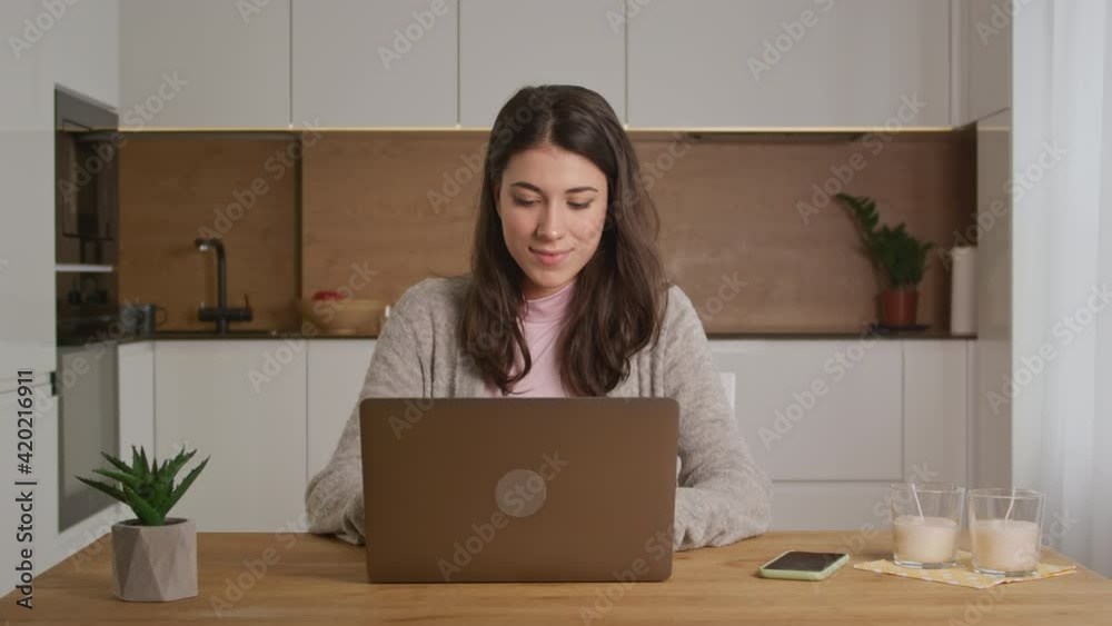 Young caucasian thoughful woman is working on a laptop at home on her kitchen in a modern apartment Young caucasian thoughful woman is working on a laptop at home on her kitchen in a modern apartment