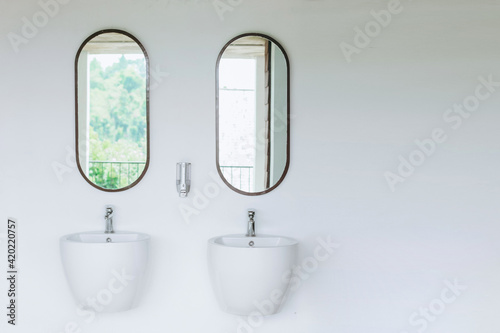 Double sink on white wall with two mirrors hanging above it