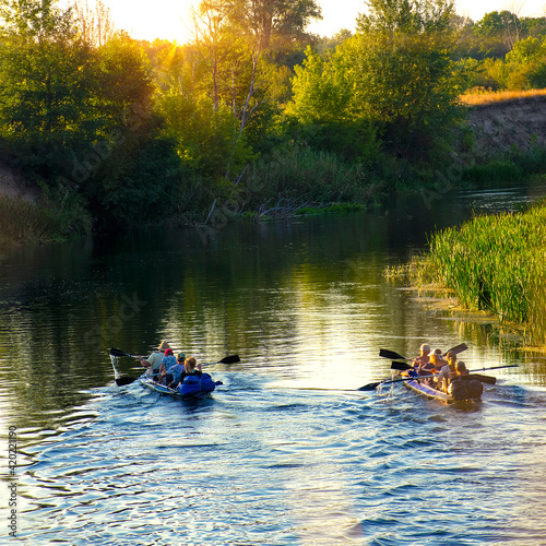Families of friends canoe down the river at sunset. Cheerful company of tourists