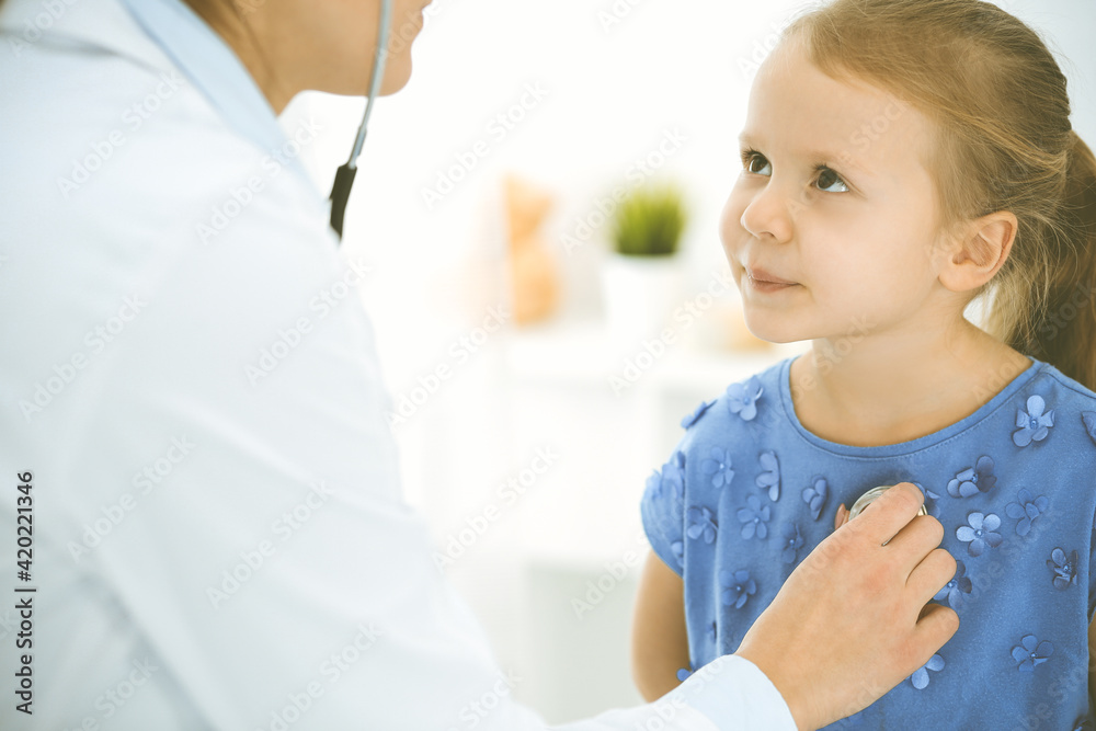 Doctor examining a child by stethoscope. Happy smiling girl patient dressed in blue dress is at usual medical inspection. Medicine concept Doctor examining a child by stethoscope. Happy smiling girl patient dressed in blue dress is at usual medical inspection. Medicine concept