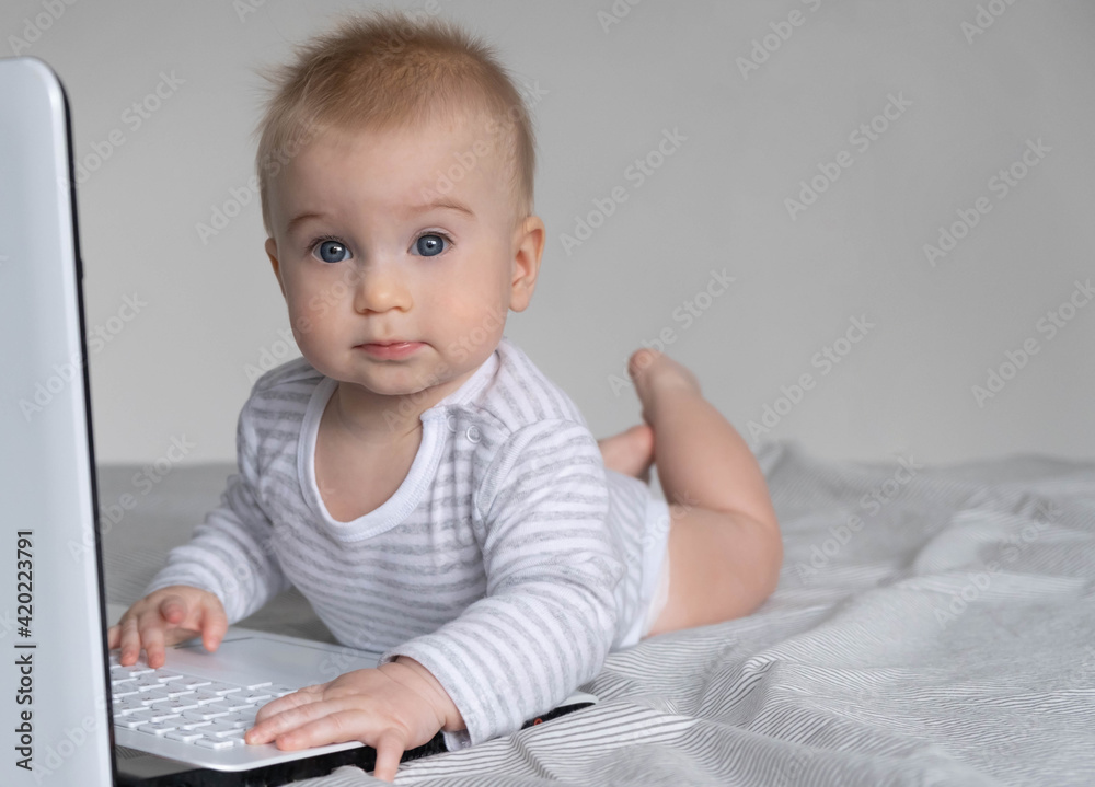 Adorable funny baby playing with keyboard of laptop, lying on bed. Early kid development and new technology concept Adorable funny baby playing with keyboard of laptop, lying on bed. Early kid development and new technology concept
