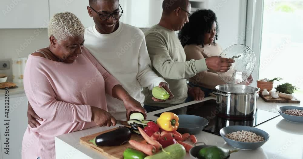 Happy african family cooking inside kitchen at home - Father, daughter, son and mother having fun preparing lunch 