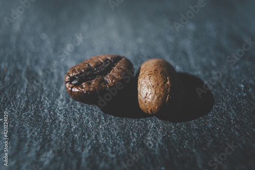 zwei Kaffee Bohnen auf einem Schiefer Stein Untergrund in stimmungsvollen Farben vor einem weichen Bokeh Hintergrund photo