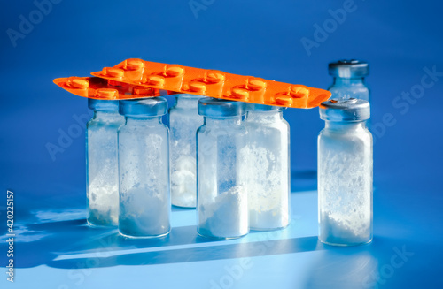 Medical bottles for injection with white powder and drug blister packs on blue background