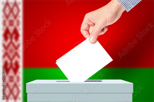 The hand of man putting his vote in the ballot box with Belarusflag on background. Election in Belarus photo