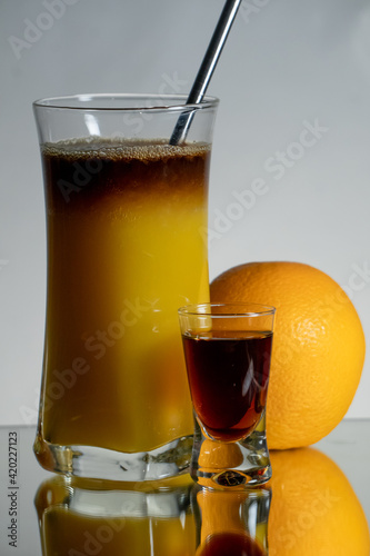 Brown, herbal layer drink with orange juice and straith metal straw. Single liqueur shot and fruit on the side. Reflection on the bottom and gradient background photo