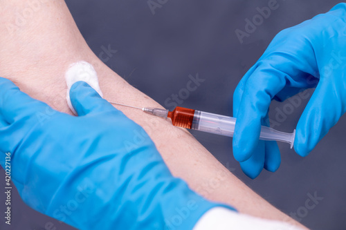 doctor in blue medical gloves giving a patient an injection into a vein in his arm