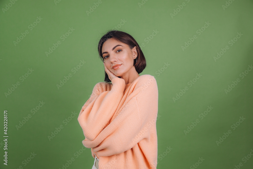 Young woman in casual peach sweater isolated on green olive color background love concept, holding hands crossed hugging herself Young woman in casual peach sweater isolated on green olive color background love concept, holding hands crossed hugging herself