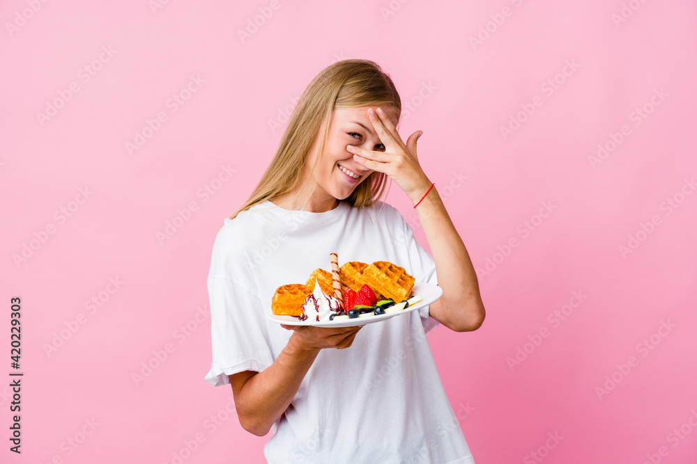 Young russian woman eating a waffle isolated blink at the camera through fingers, embarrassed covering face. Young russian woman eating a waffle isolated blink at the camera through fingers, embarrassed covering face.