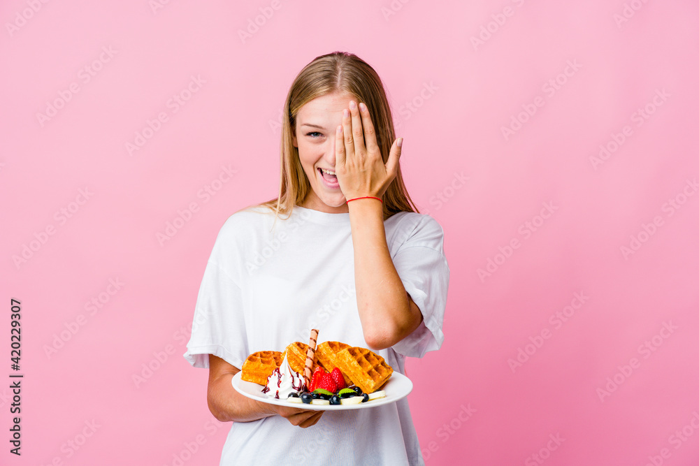 Young russian woman eating a waffle isolated having fun covering half of face with palm. Young russian woman eating a waffle isolated having fun covering half of face with palm.