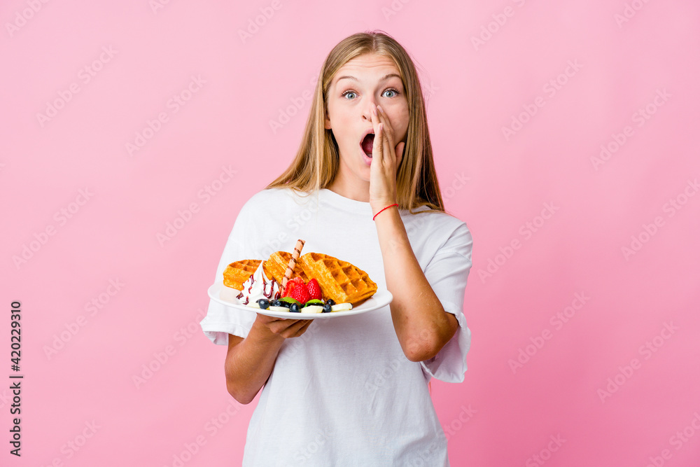 Young russian woman eating a waffle isolated shouting excited to front.