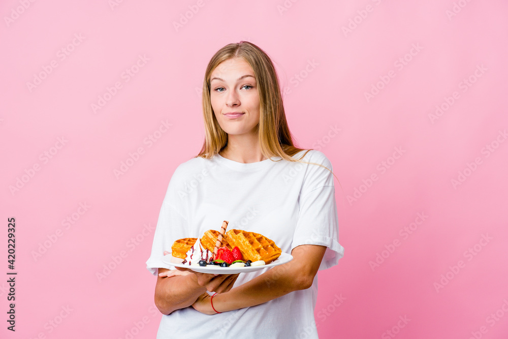 Young russian woman eating a waffle isolated who feels confident, crossing arms with determination. Young russian woman eating a waffle isolated who feels confident, crossing arms with determination.