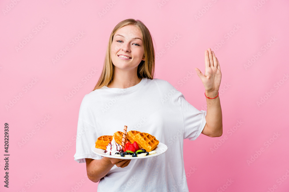 Young russian woman eating a waffle isolated smiling cheerful showing number five with fingers. Young russian woman eating a waffle isolated smiling cheerful showing number five with fingers.