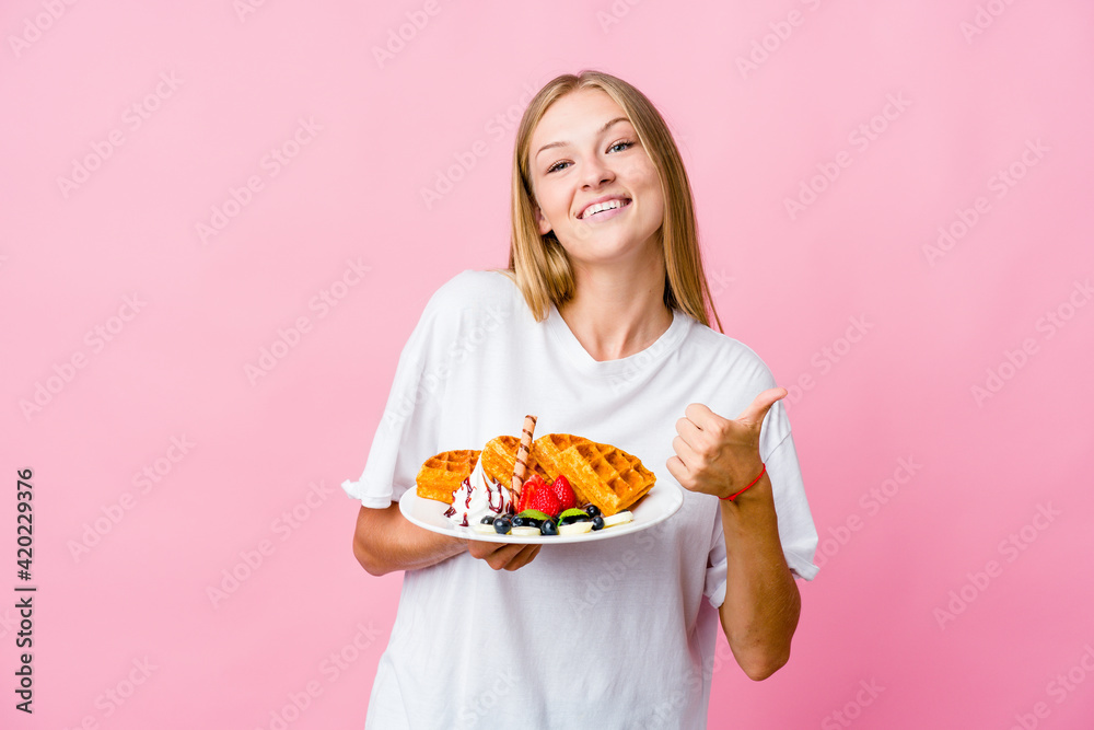 Young russian woman eating a waffle isolated raising both thumbs up, smiling and confident.