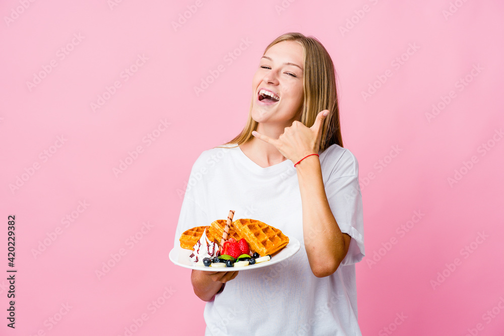 Young russian woman eating a waffle isolated showing a mobile phone call gesture with fingers. Young russian woman eating a waffle isolated showing a mobile phone call gesture with fingers.