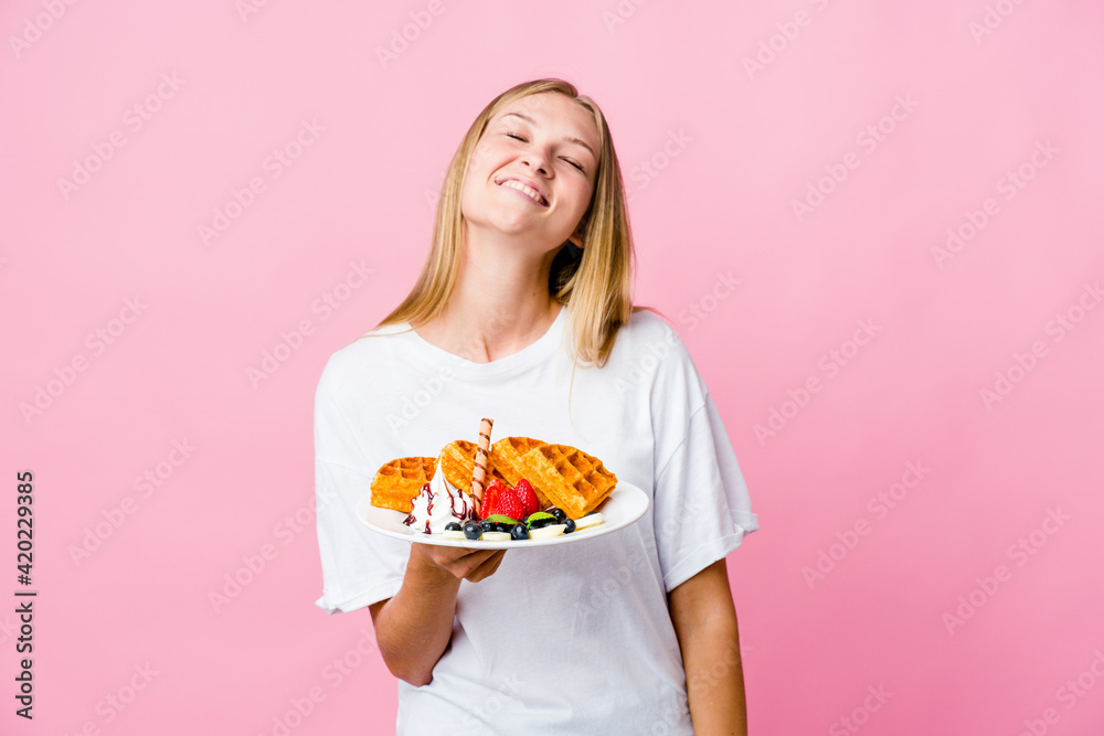 Young russian woman eating a waffle isolated relaxed and happy laughing, neck stretched showing teeth.