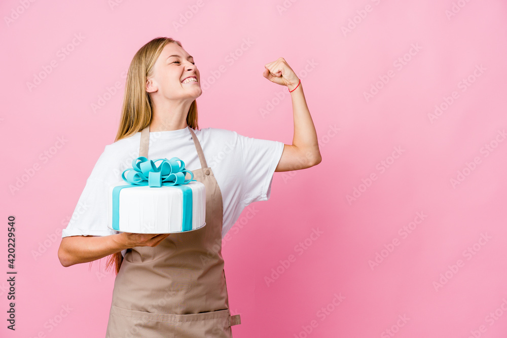 Young russian baker woman holding a delicious cake raising fist after a victory, winner concept. Young russian baker woman holding a delicious cake raising fist after a victory, winner concept.