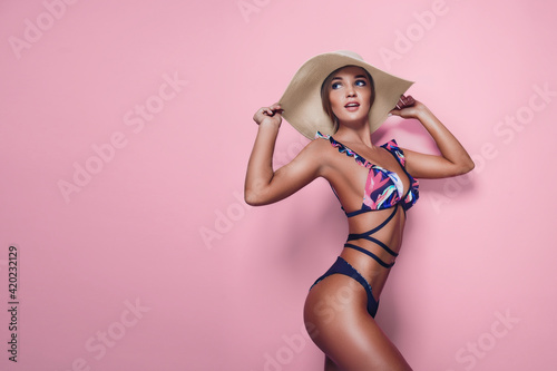 Charming blond girl in one-piece swimsuit and straw hat