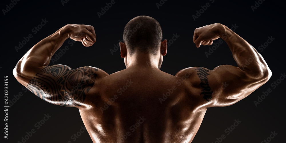 Male bodybuilder with light stubble with a naked torso posing against a dark background. The concept of a fitness club, doing sports, weightlifting. Copy space.