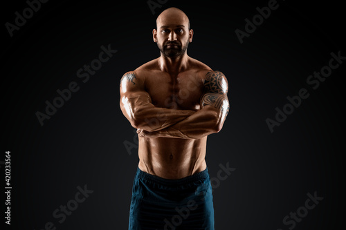 Male bodybuilder with light stubble with a naked torso posing against a dark background. The concept of a fitness club, doing sports, weightlifting. Copy space.
