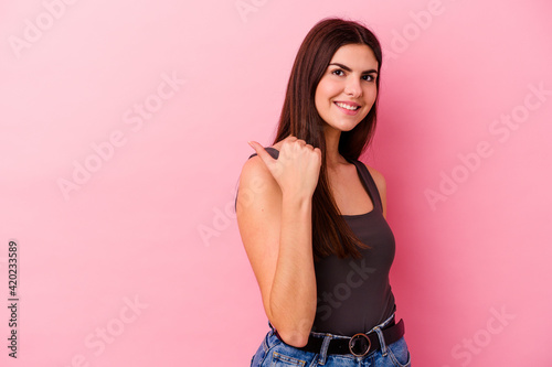 Young caucasian woman isolated on pink background points with thumb finger away  laughing and carefree.