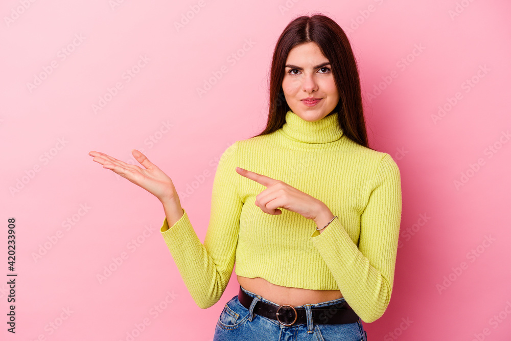 Young caucasian woman isolated on pink background excited holding a copy space on palm. Young caucasian woman isolated on pink background excited holding a copy space on palm.