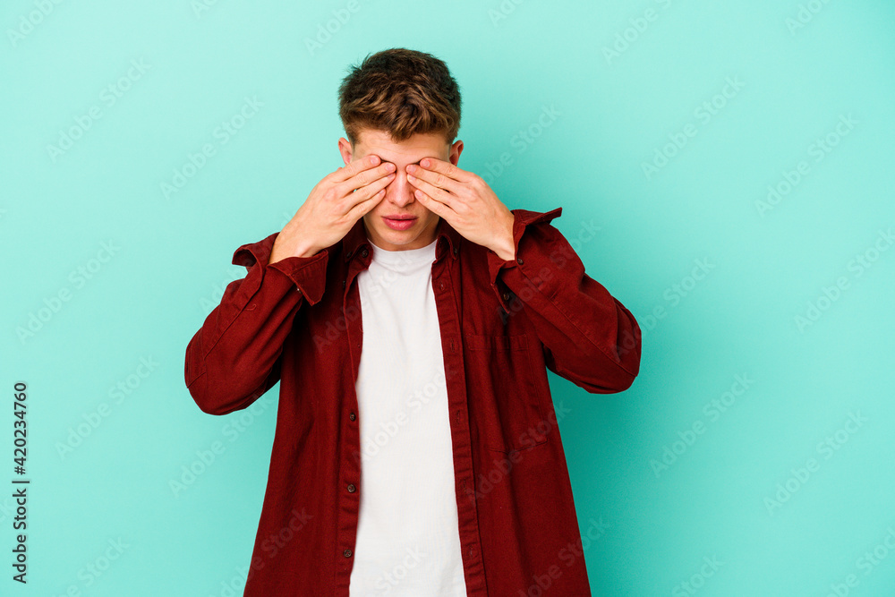 Young caucasian man isolated on blue background afraid covering eyes with hands.