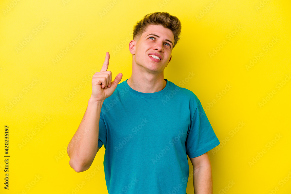 Young caucasian man isolated on yellow background indicates with both fore fingers up showing a blank space. Young caucasian man isolated on yellow background indicates with both fore fingers up showing a blank space.